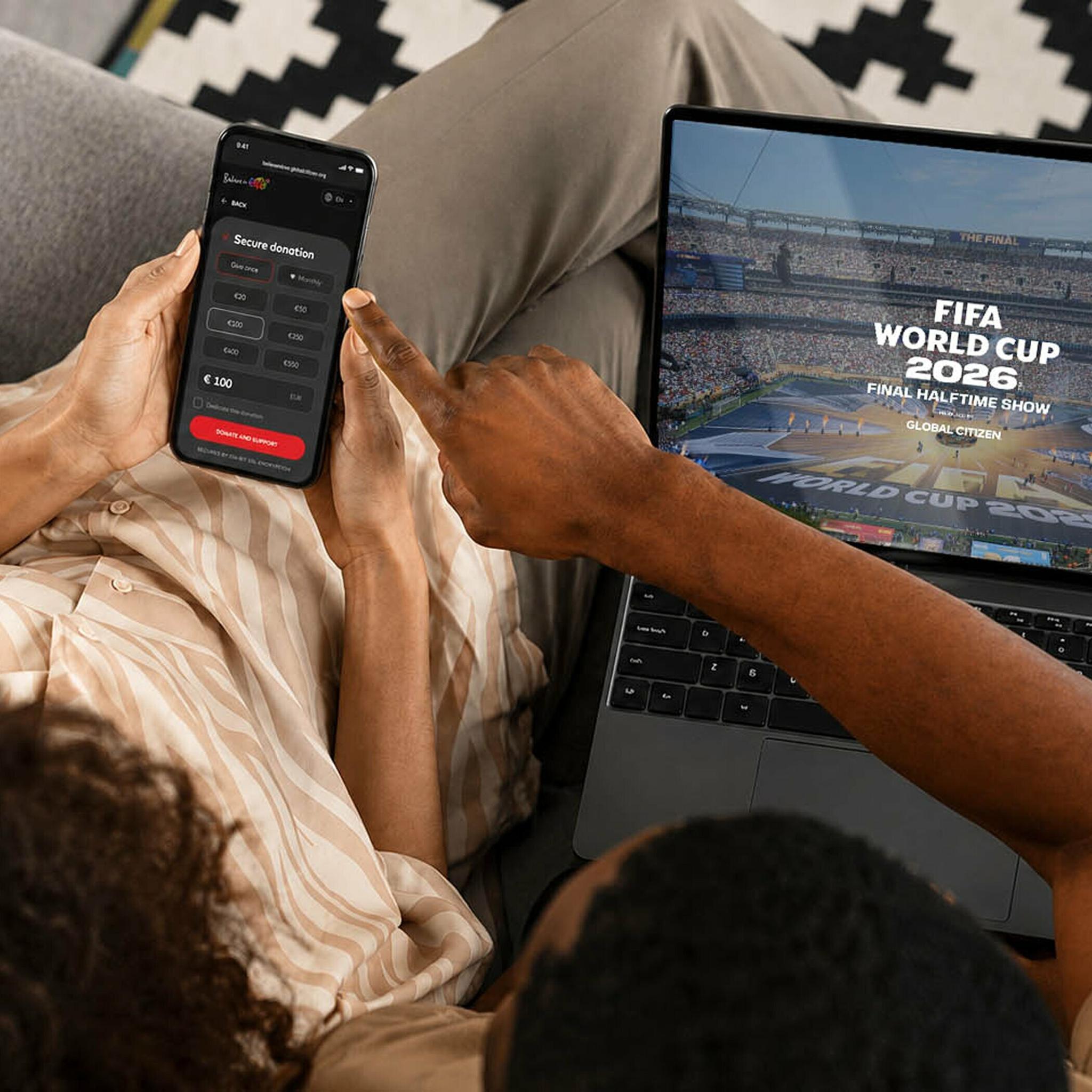 Person holds a phone beside a laptop showing a FIFA World Cup screen.