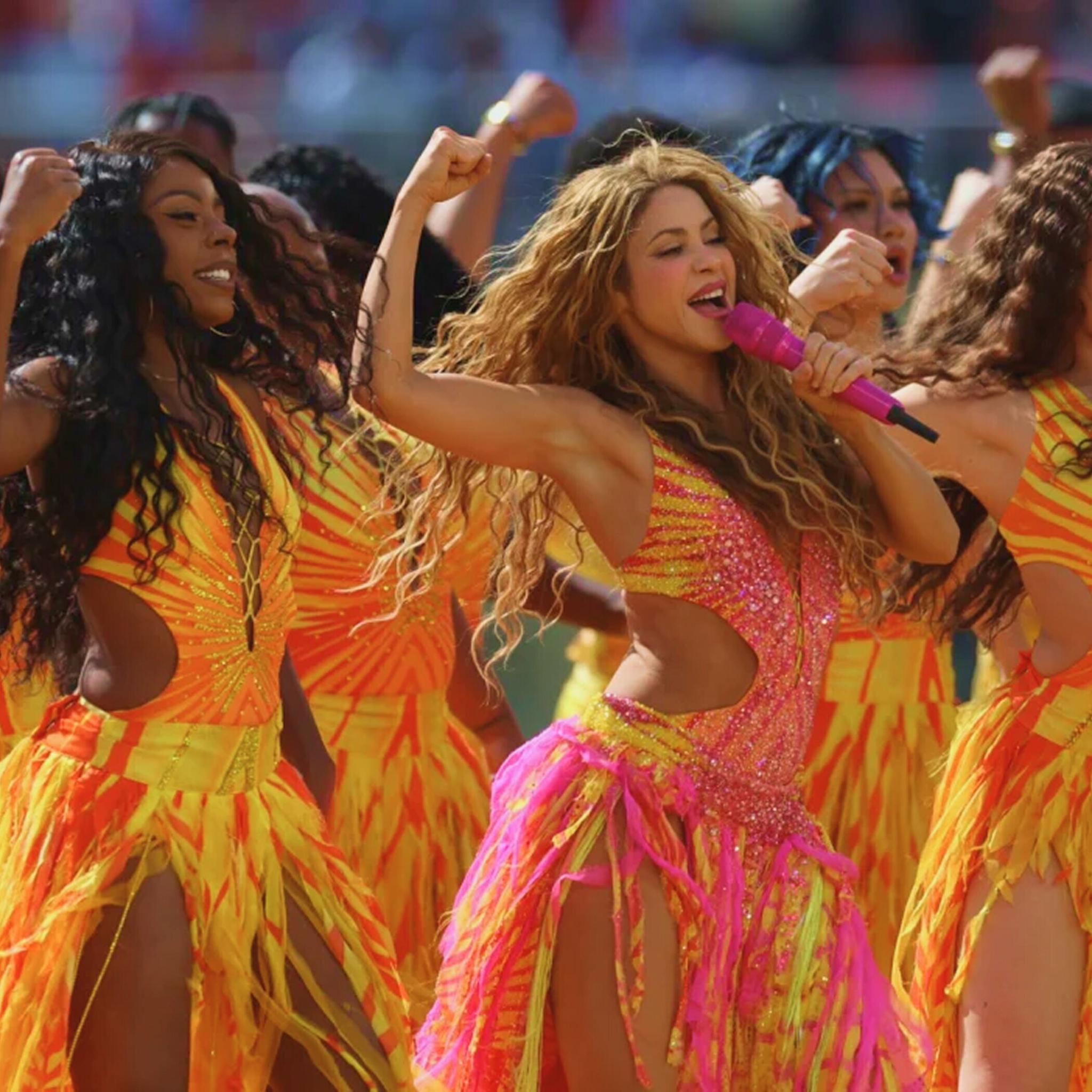 Dancers in bright costumes perform on a stadium field.