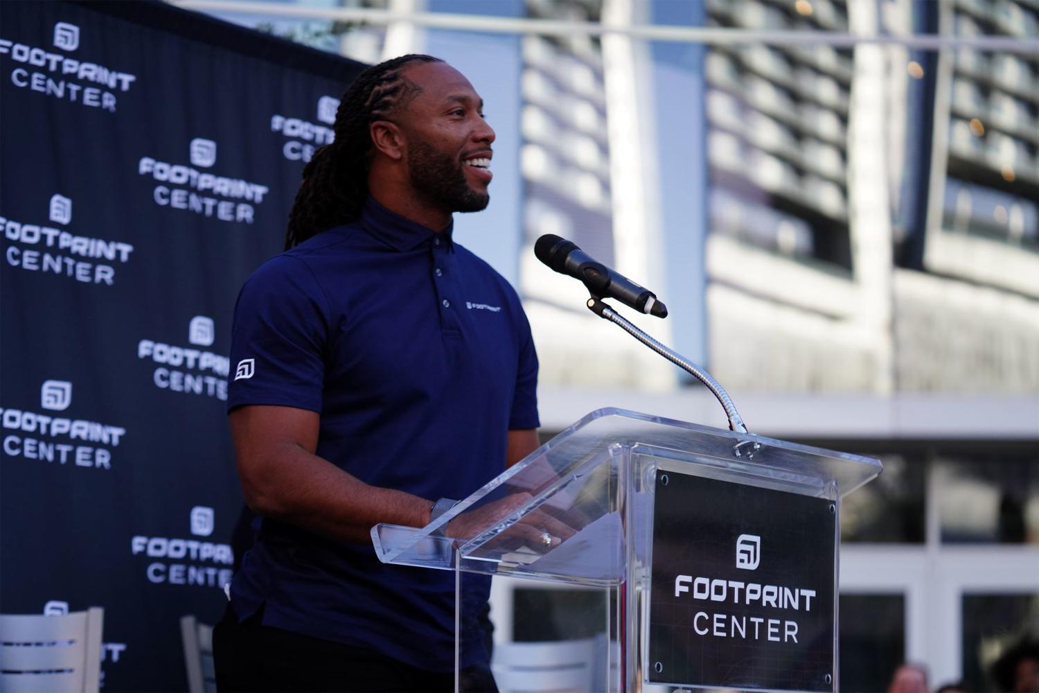 Man speaking at a Footprint Center podium during an outdoor event.