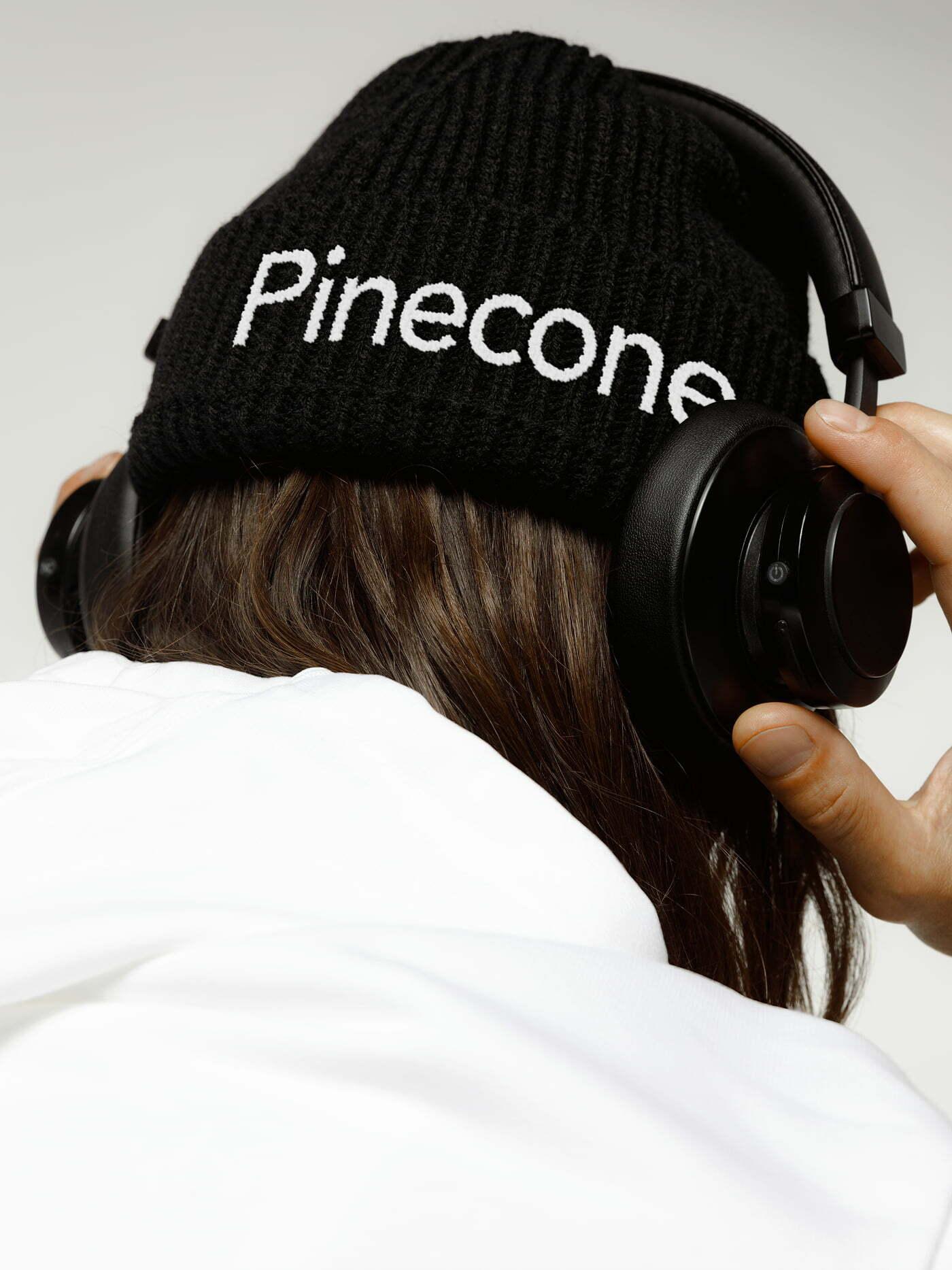Person wearing headphones and a black Pinecone beanie