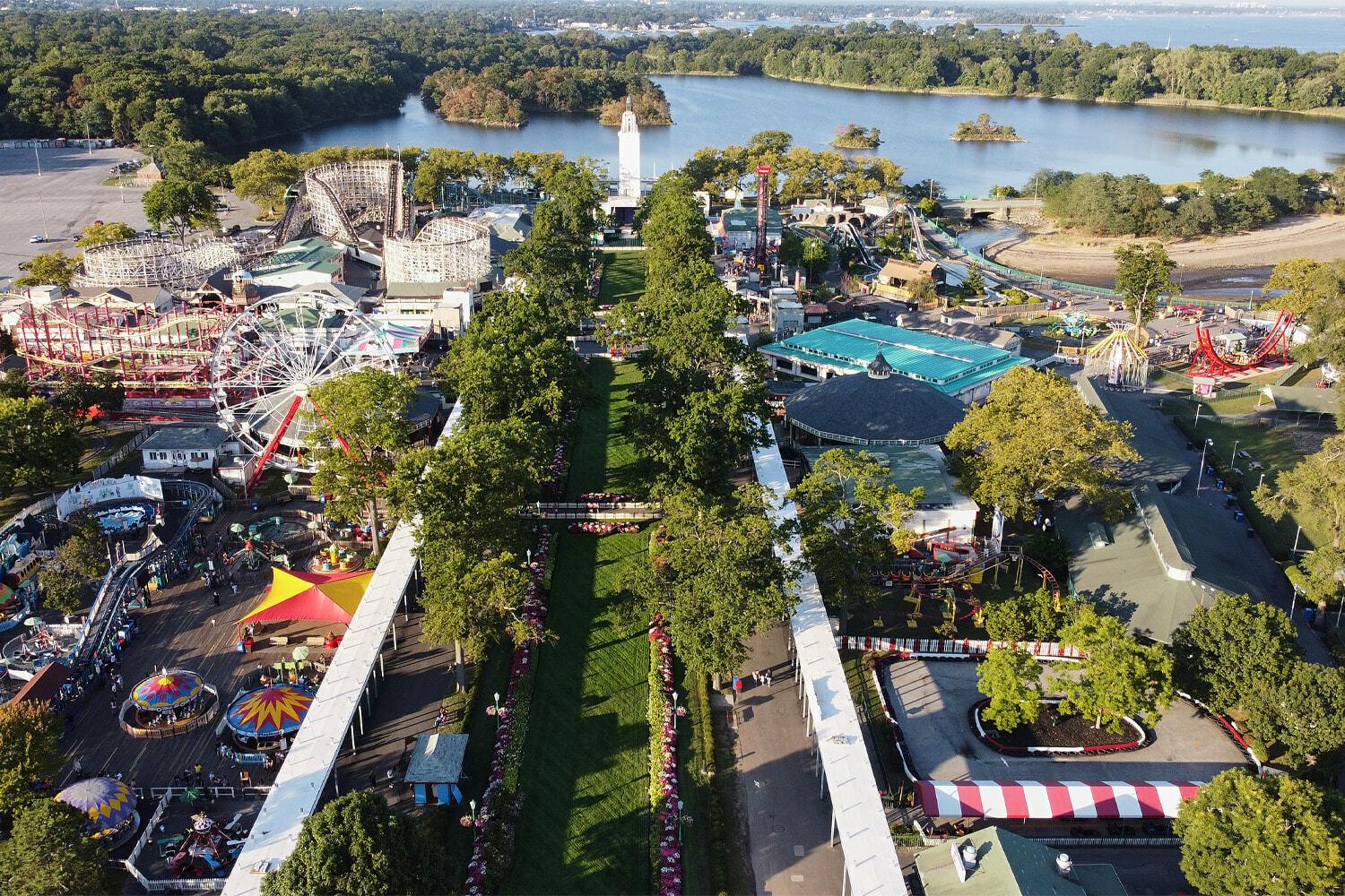 Wide aerial view of an amusement park, lake, roller coaster, and midway