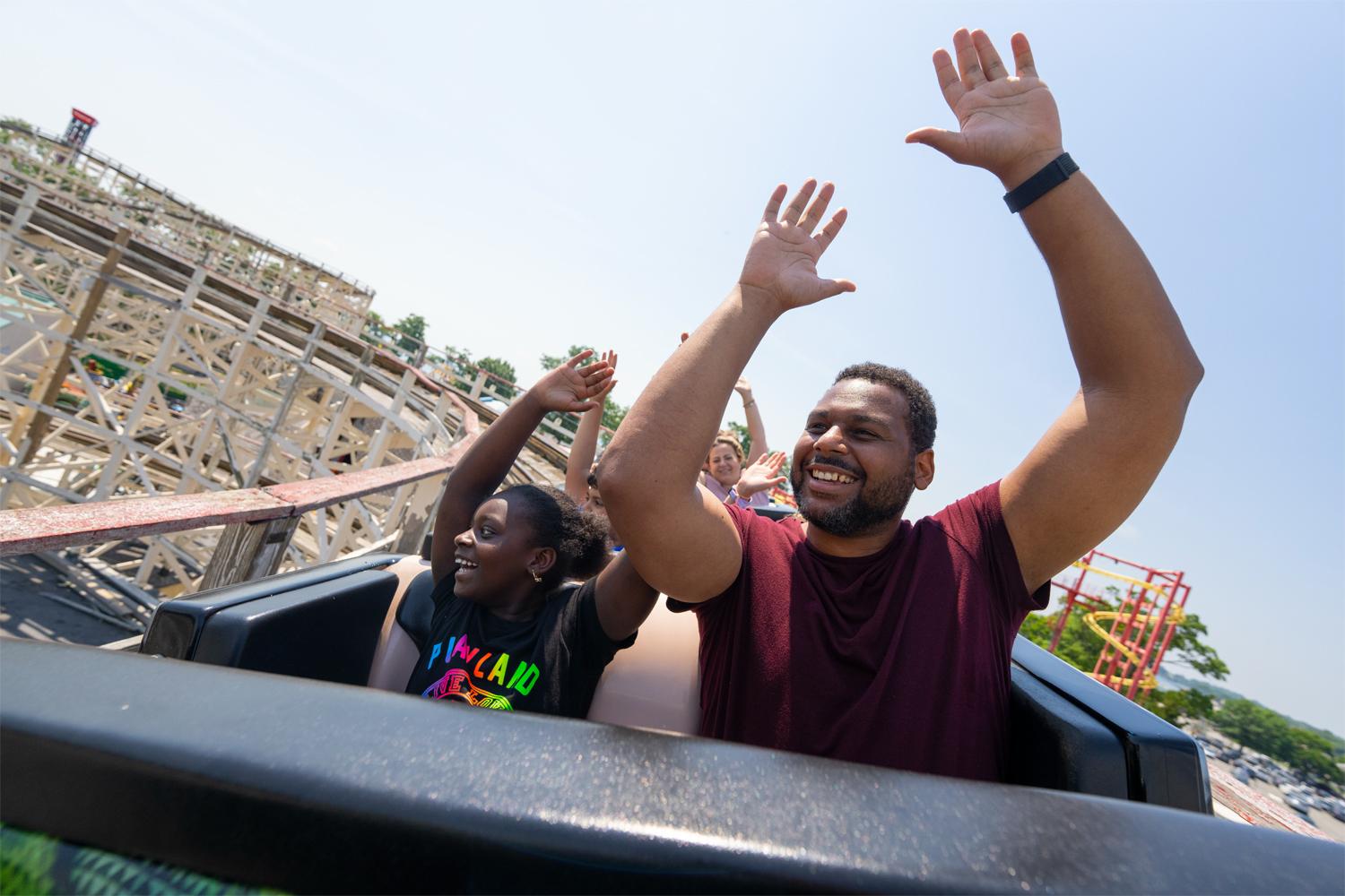 Roller coaster riders raising their hands on a wooden coaster track