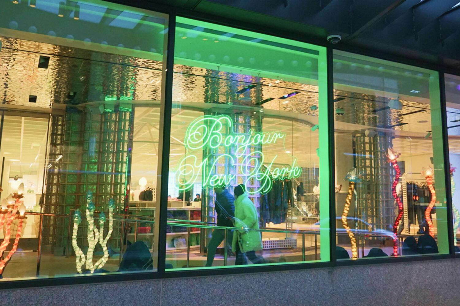 Wide storefront windows with green neon "Bonjour New York" sign inside