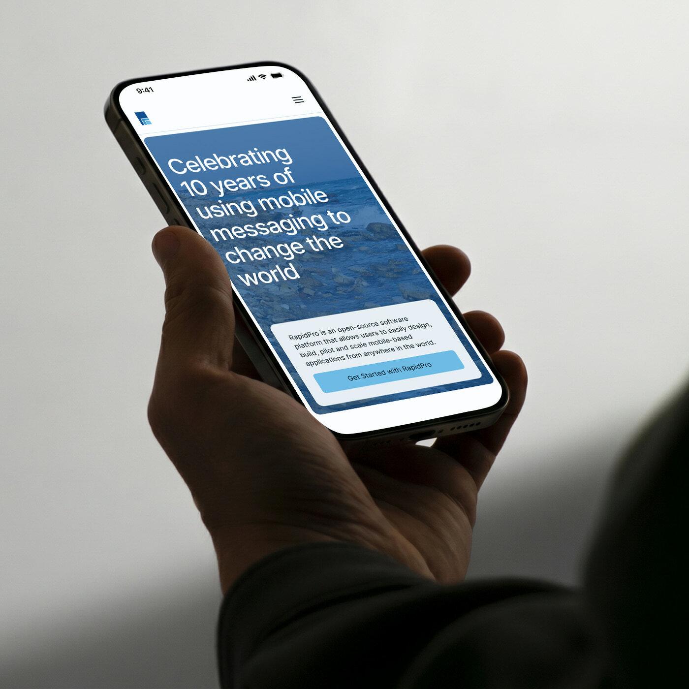 Hand holding a smartphone showing a RapidPro anniversary page.
