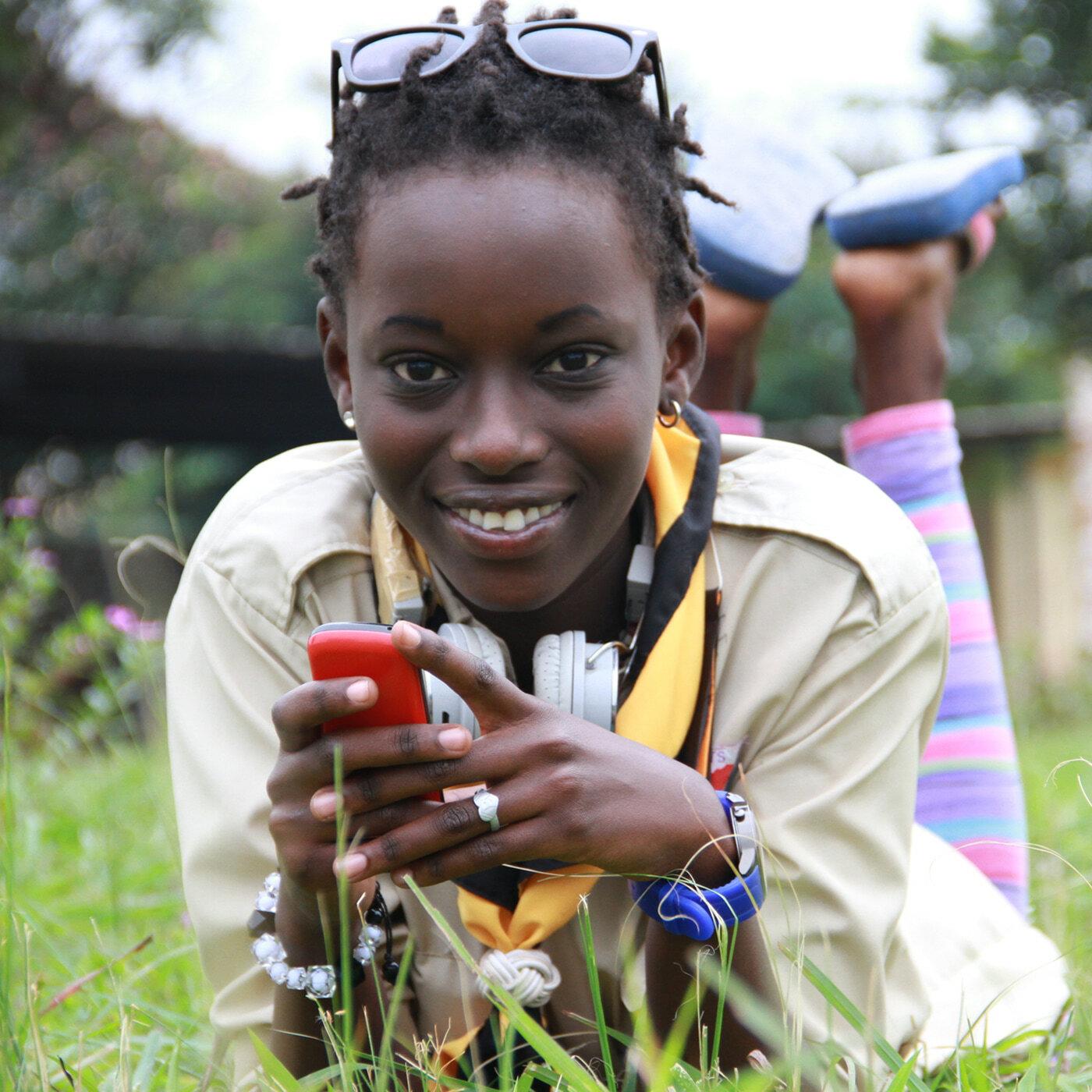 Smiling young woman lying in grass holding a red phone.