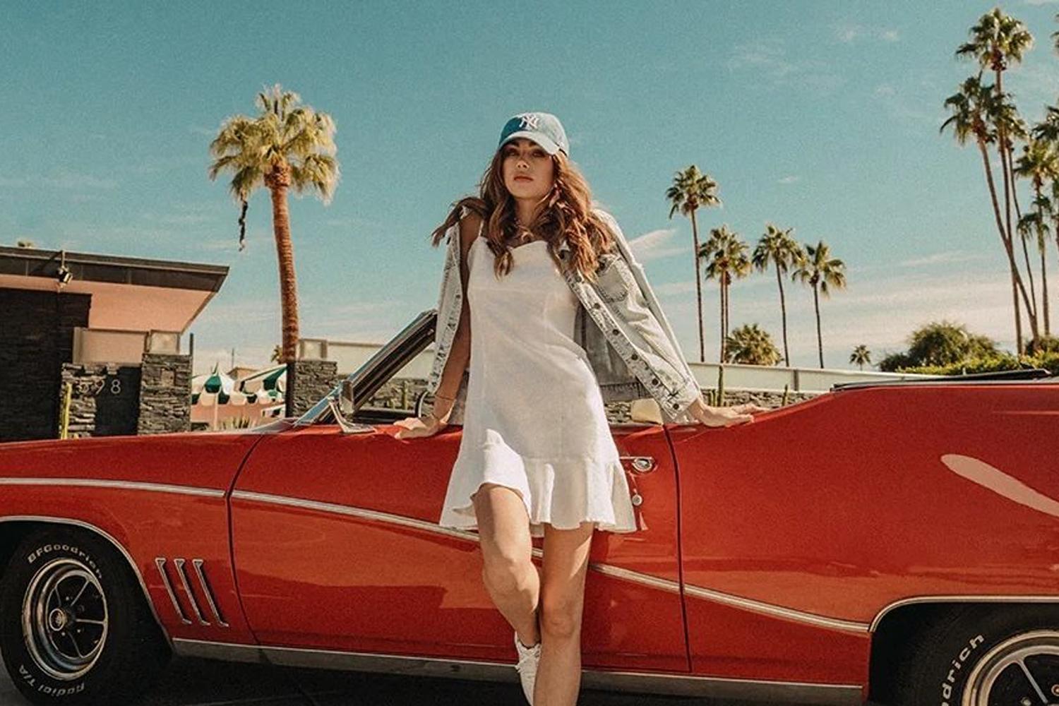Person leaning on a red convertible with palm trees in the background