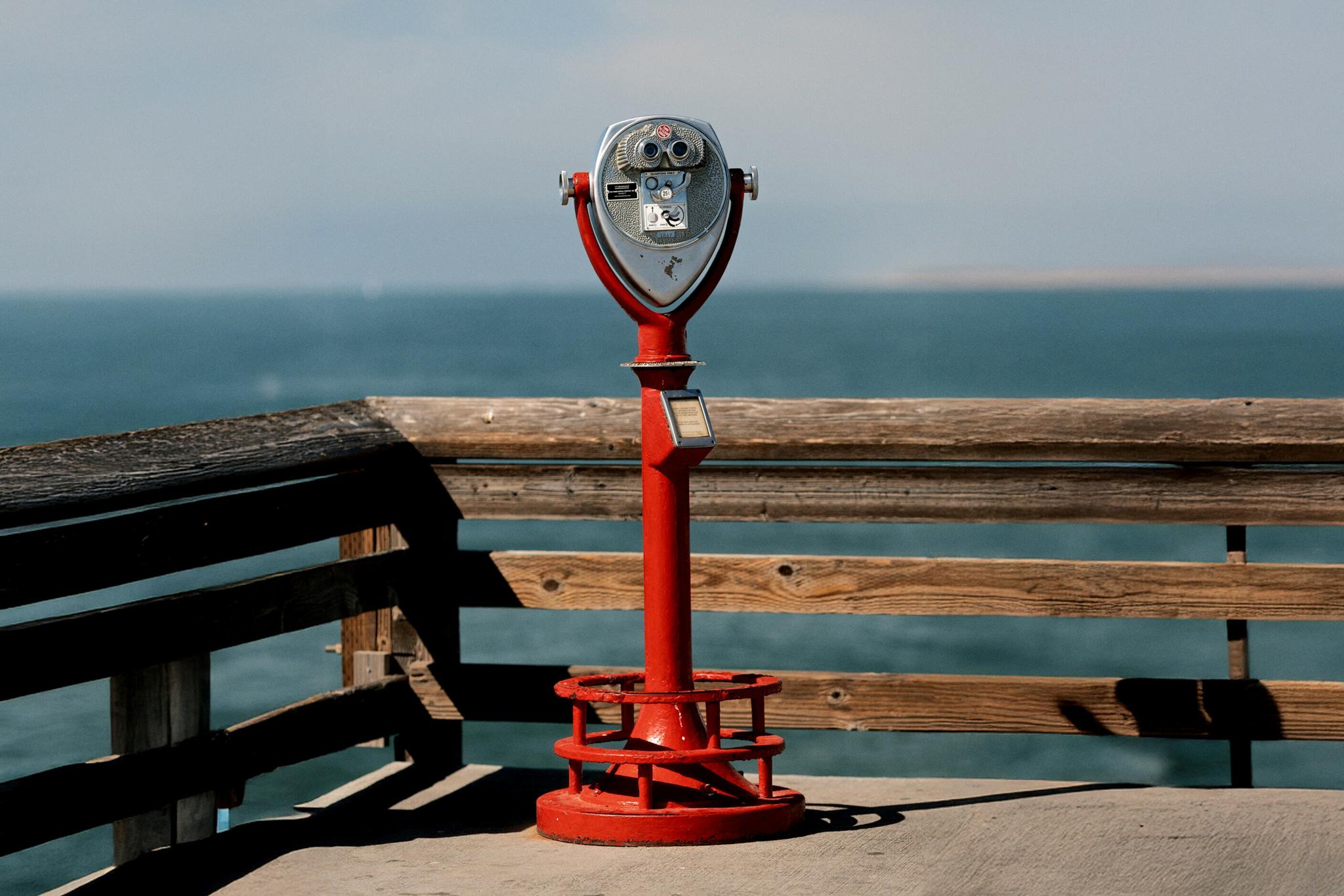 Red coin-operated binocular viewer on a pier overlooking the water.