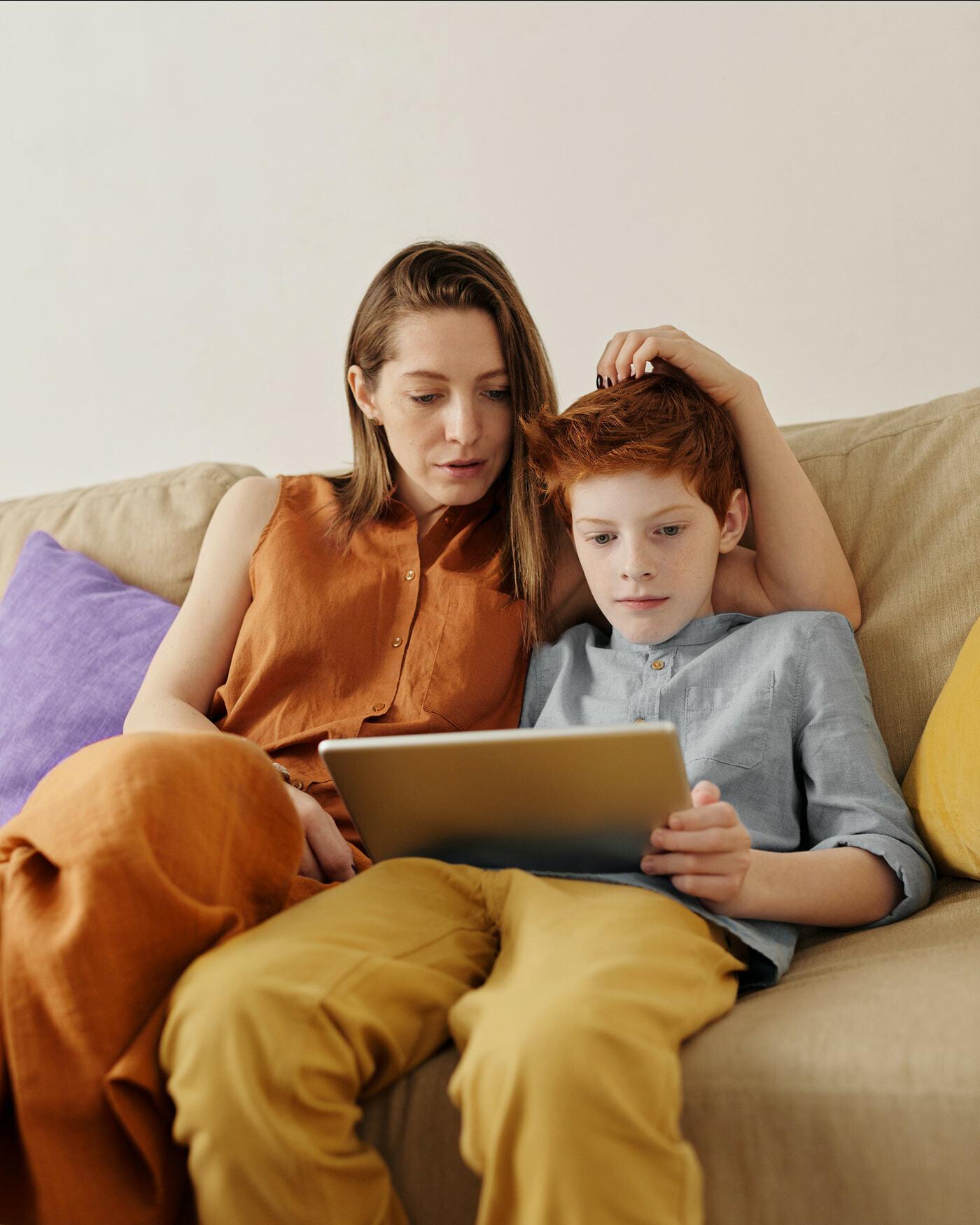 Adult and child sitting on a couch looking at a tablet