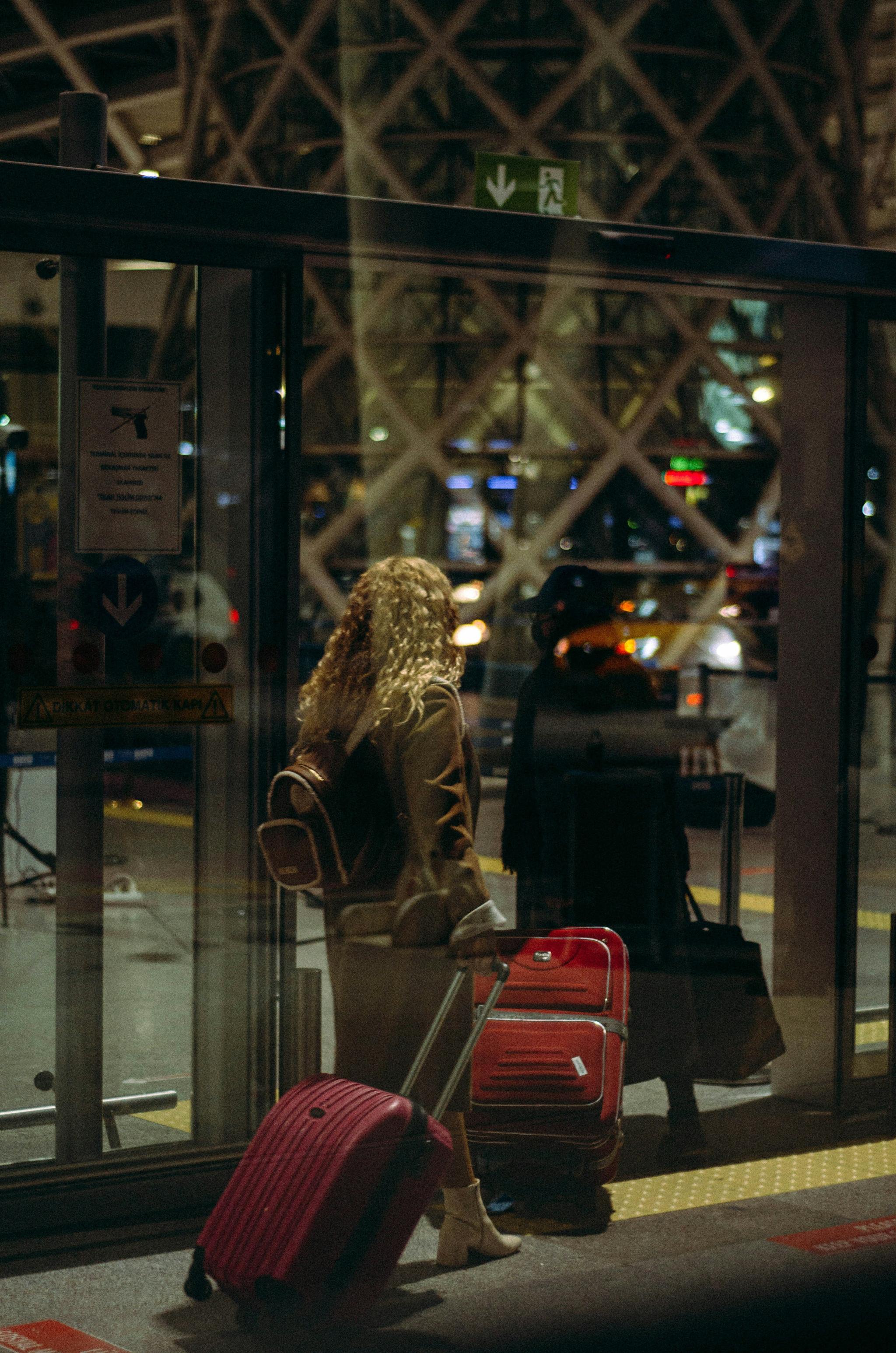 Traveler with red suitcases waiting by glass airport doors at night