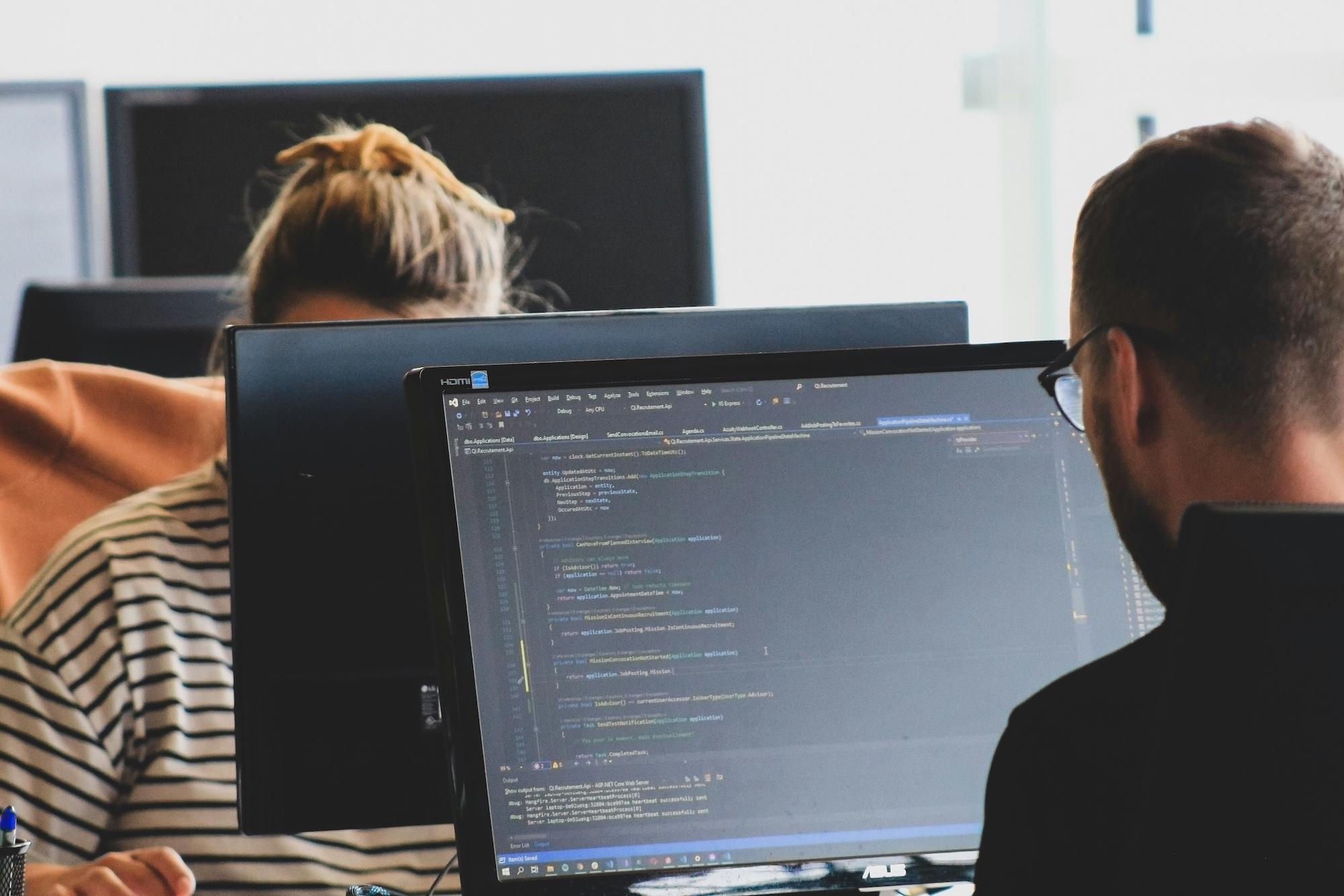 People working at computers with code visible on a monitor