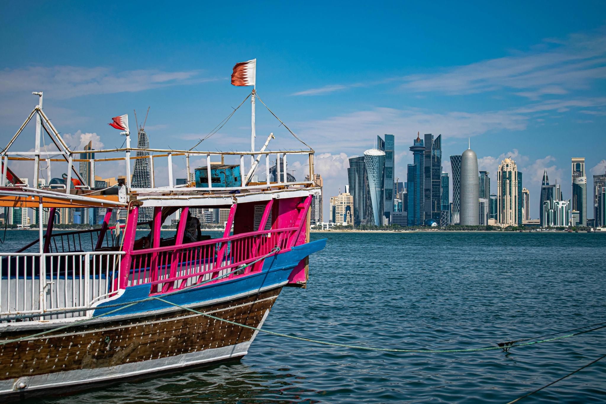 Traditional dhow boat with a Qatari flag on the water, Doha skyline behind