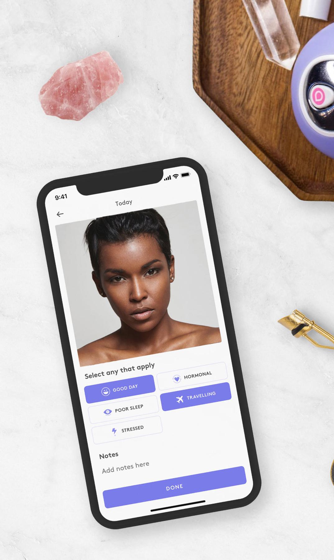 Phone showing a skincare tracking app beside beauty tools and a purple device