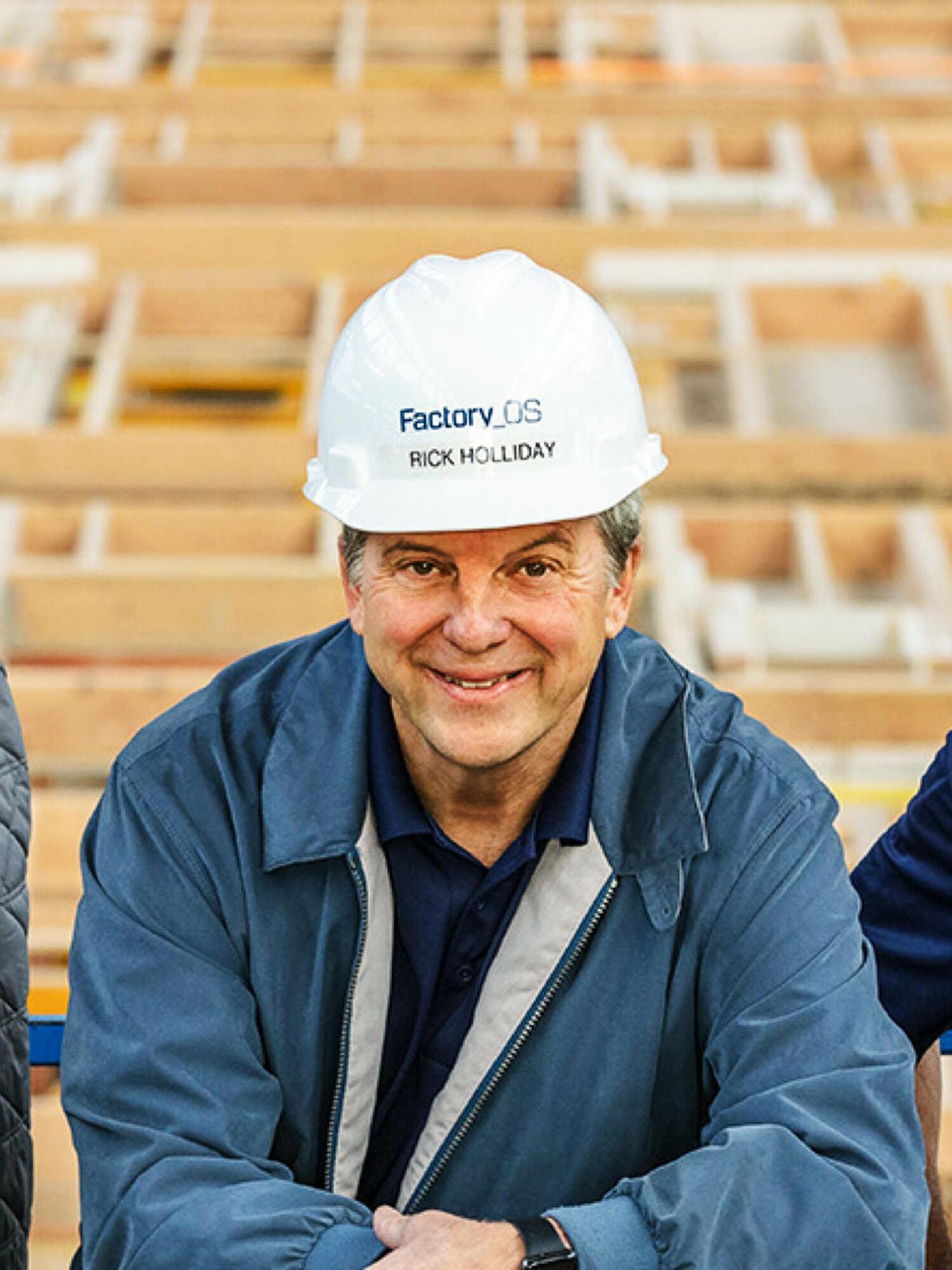 Smiling construction worker wearing a Factory OS hard hat in front of framing