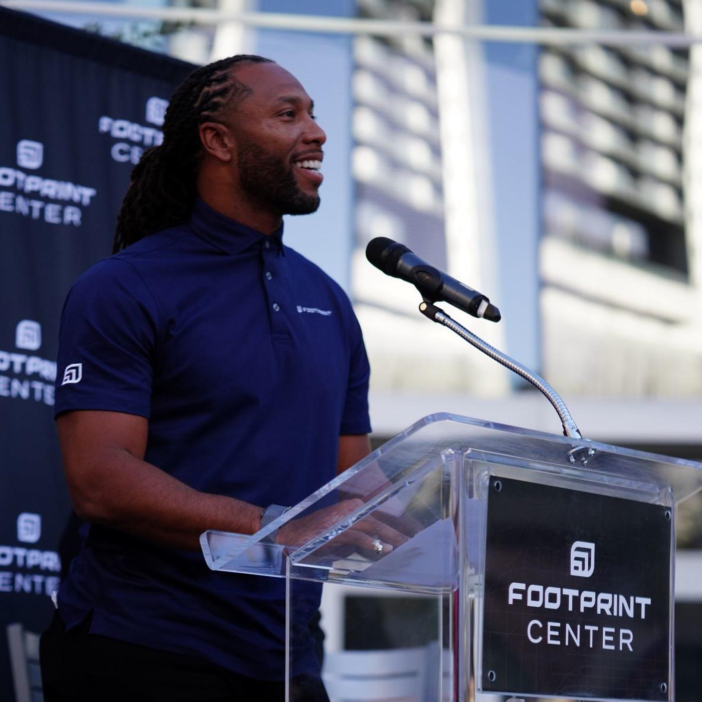 Man speaking at a Footprint Center podium with a microphone outdoors