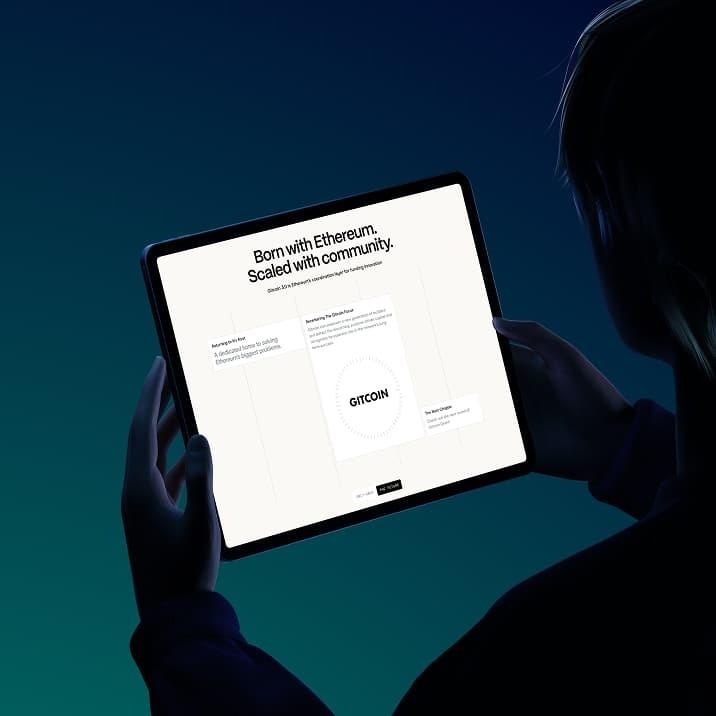 Person holds a tablet displaying a Gitcoin page with "Born with Ethereum. Scaled with community."
