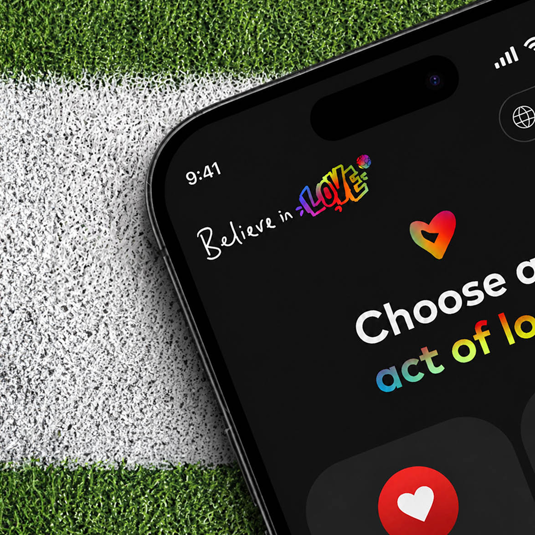 Phone on turf showing a Believe in Love campaign screen.