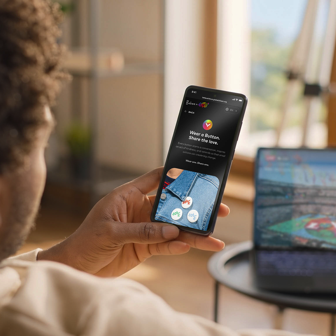 Person holding a phone with a dark campaign app screen beside a laptop.