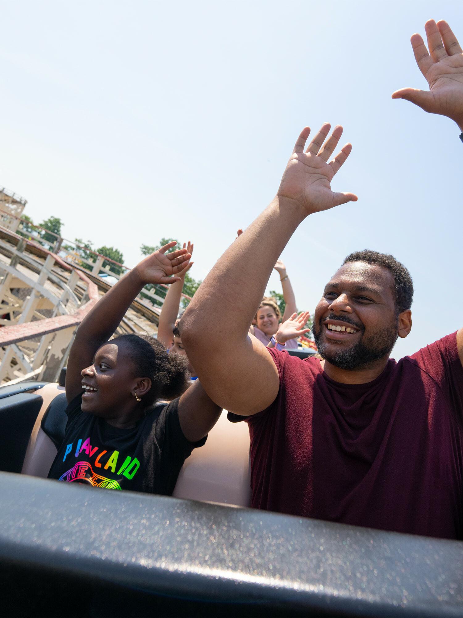 Roller coaster riders smiling with hands raised on a sunny day