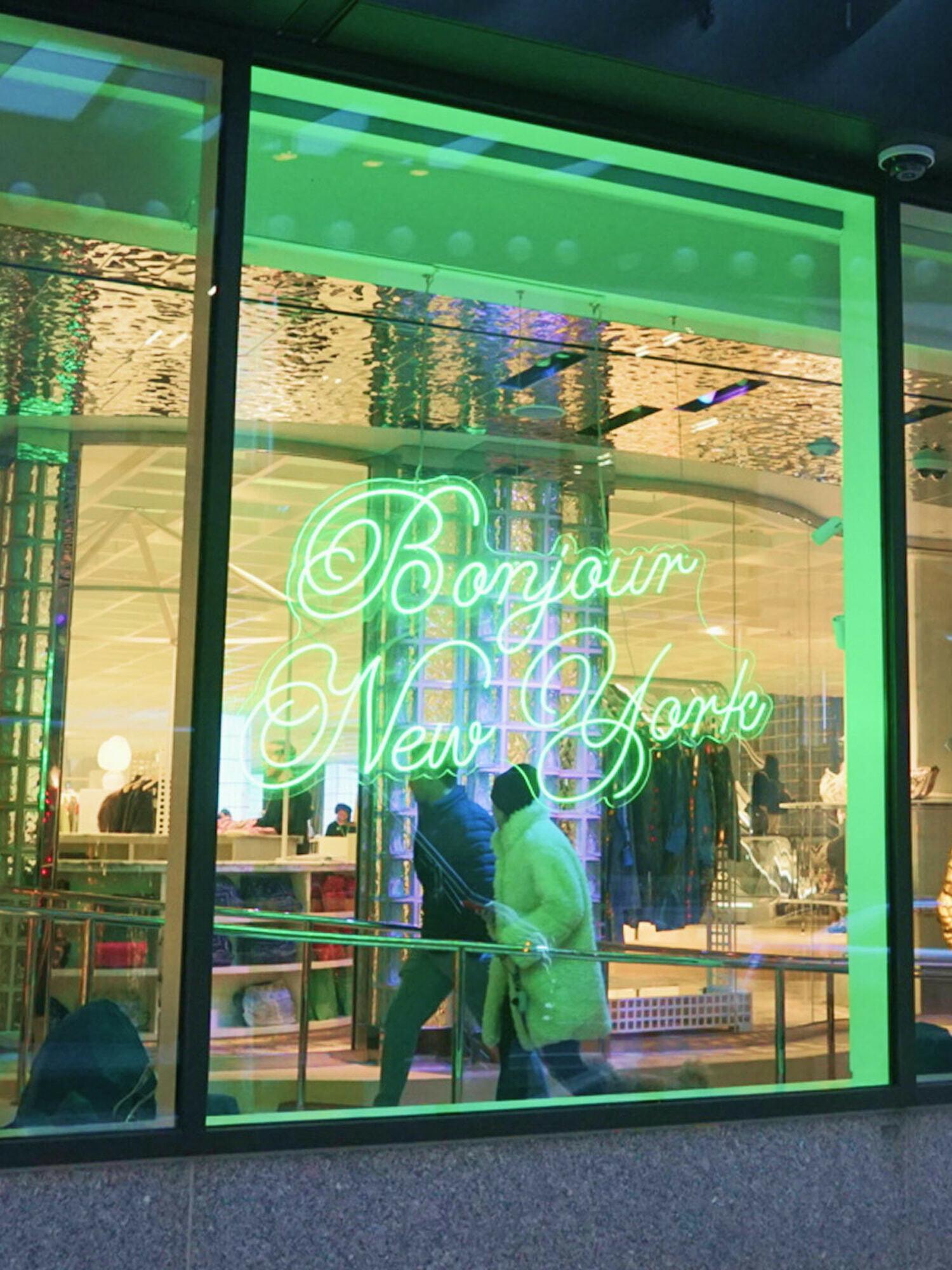 Storefront window with green neon sign reading "Bonjour New York"