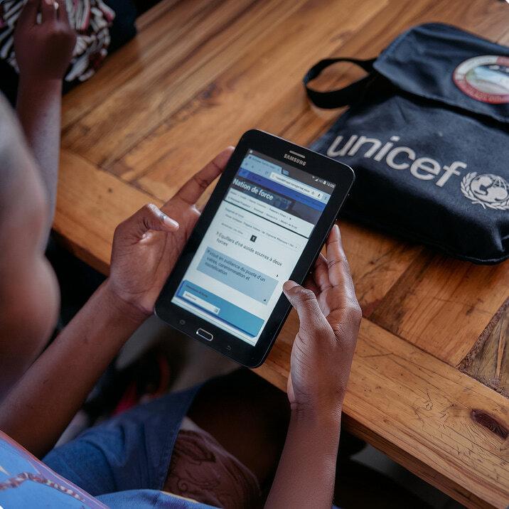 Person using a tablet beside a UNICEF bag on a wooden table.