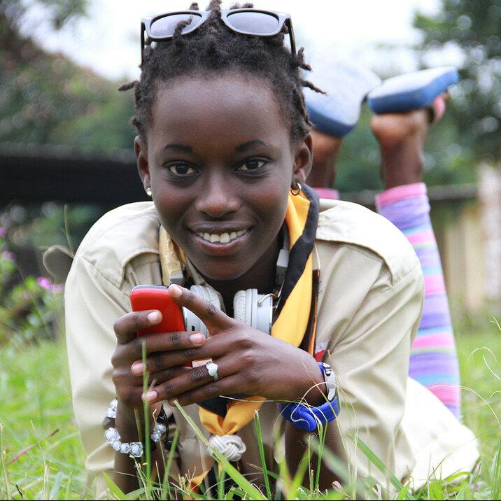Smiling young woman lying in grass holding a red phone.