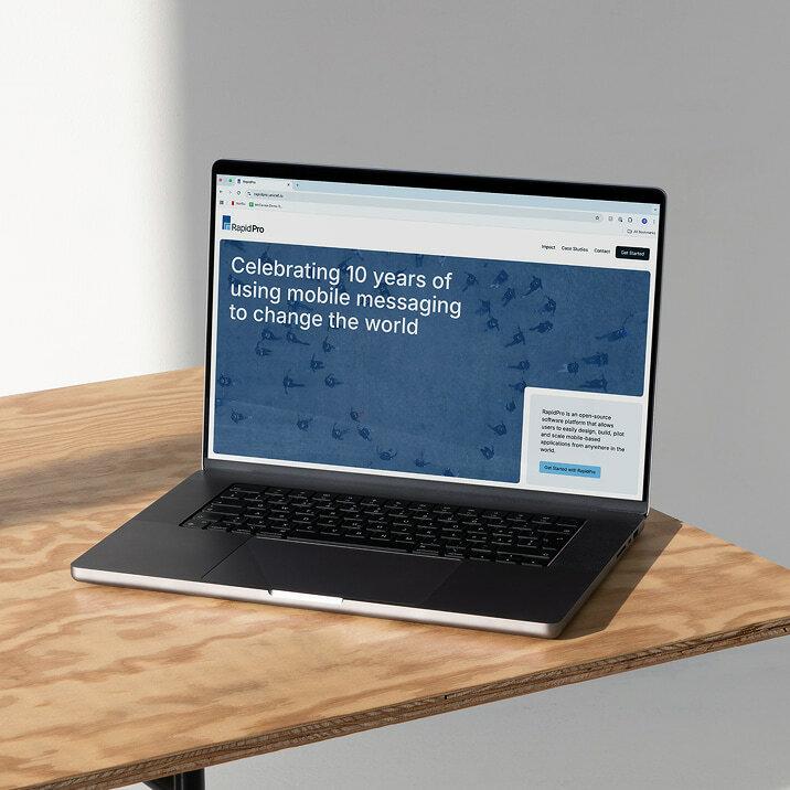 Laptop showing a RapidPro website mockup on a wooden table.