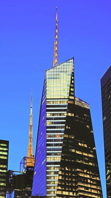 Angular glass skyscraper with a lit spire against a blue evening sky