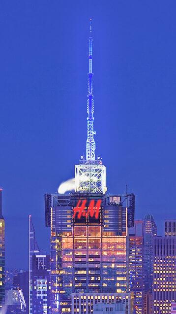 City skyscraper with a large H&M sign and rooftop antenna at dusk