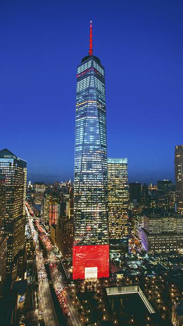 One World Trade Center lit at night with a red base and city skyline