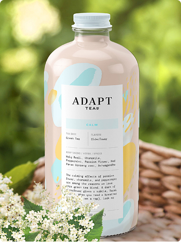 Adapt Tea Calm bottle with pastel label, flowers, and a wicker basket in greenery