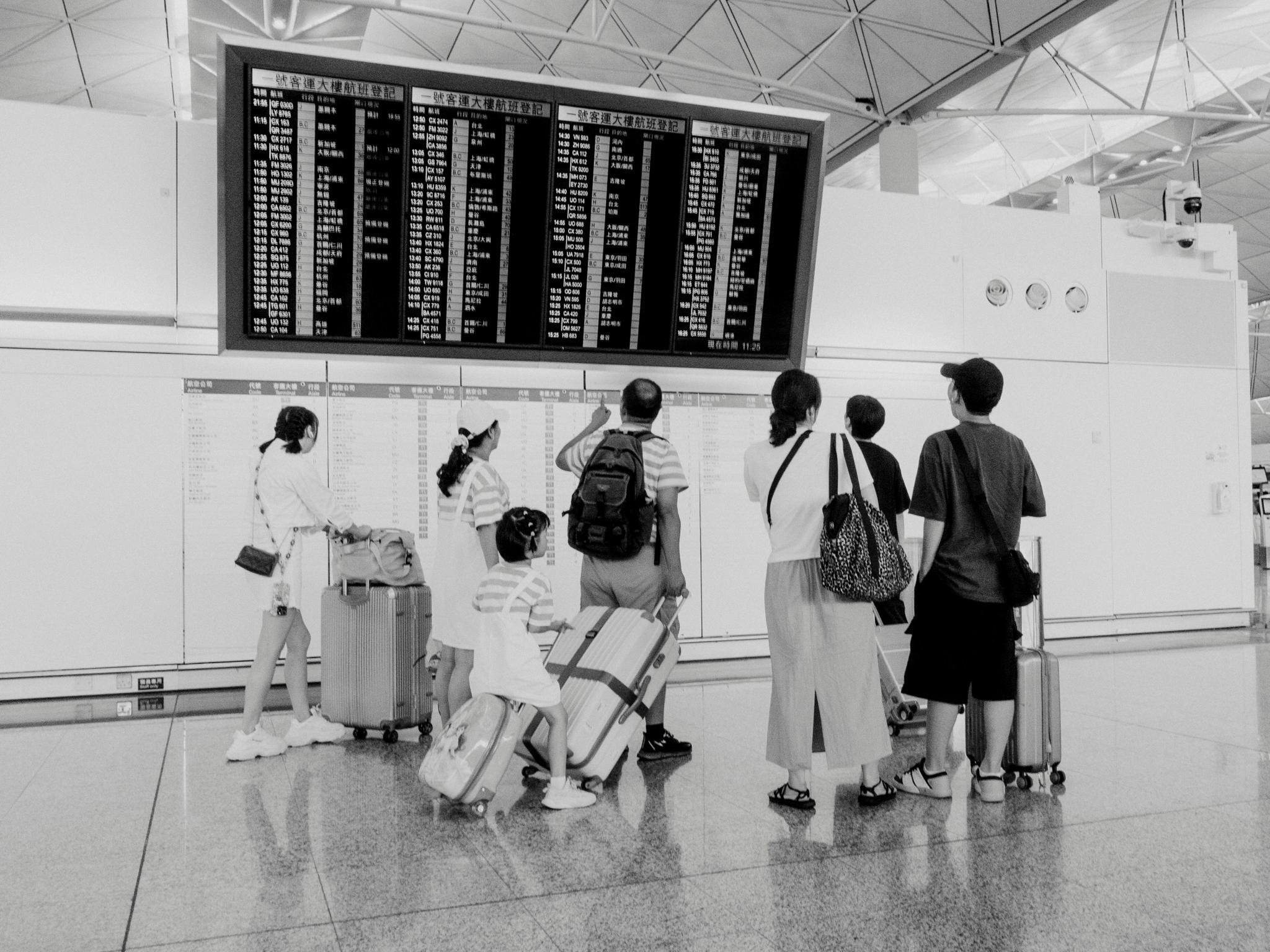 Black-and-white airport scene with travelers viewing a flight board