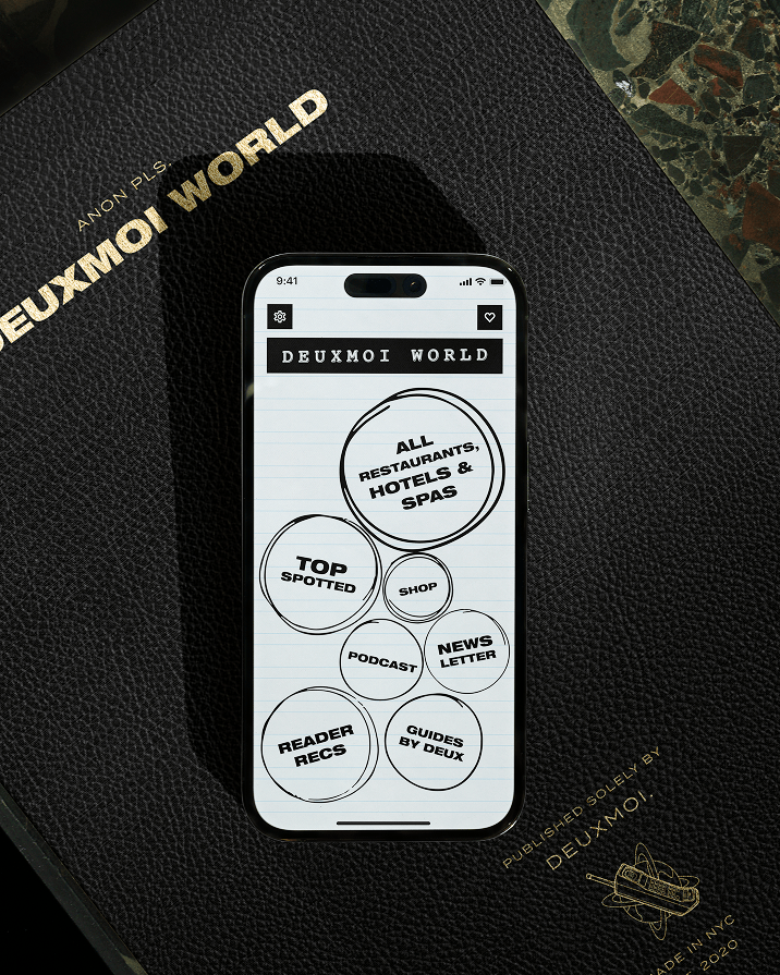 Phone showing Deuxmoi World app menu on a black leather book
