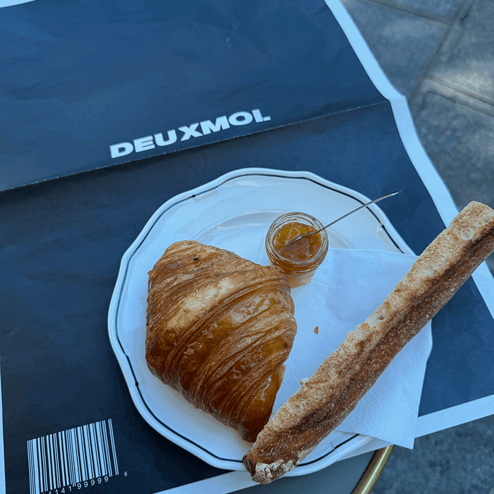 Croissant, breadstick, and jam on a plate over a DEUXMOI magazine
