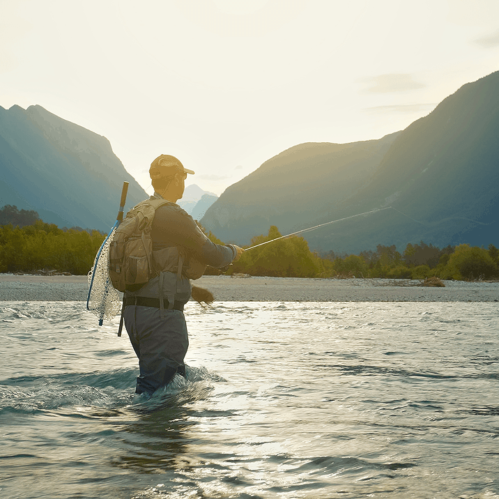 Angler fly fishing in a river with mountains in the background