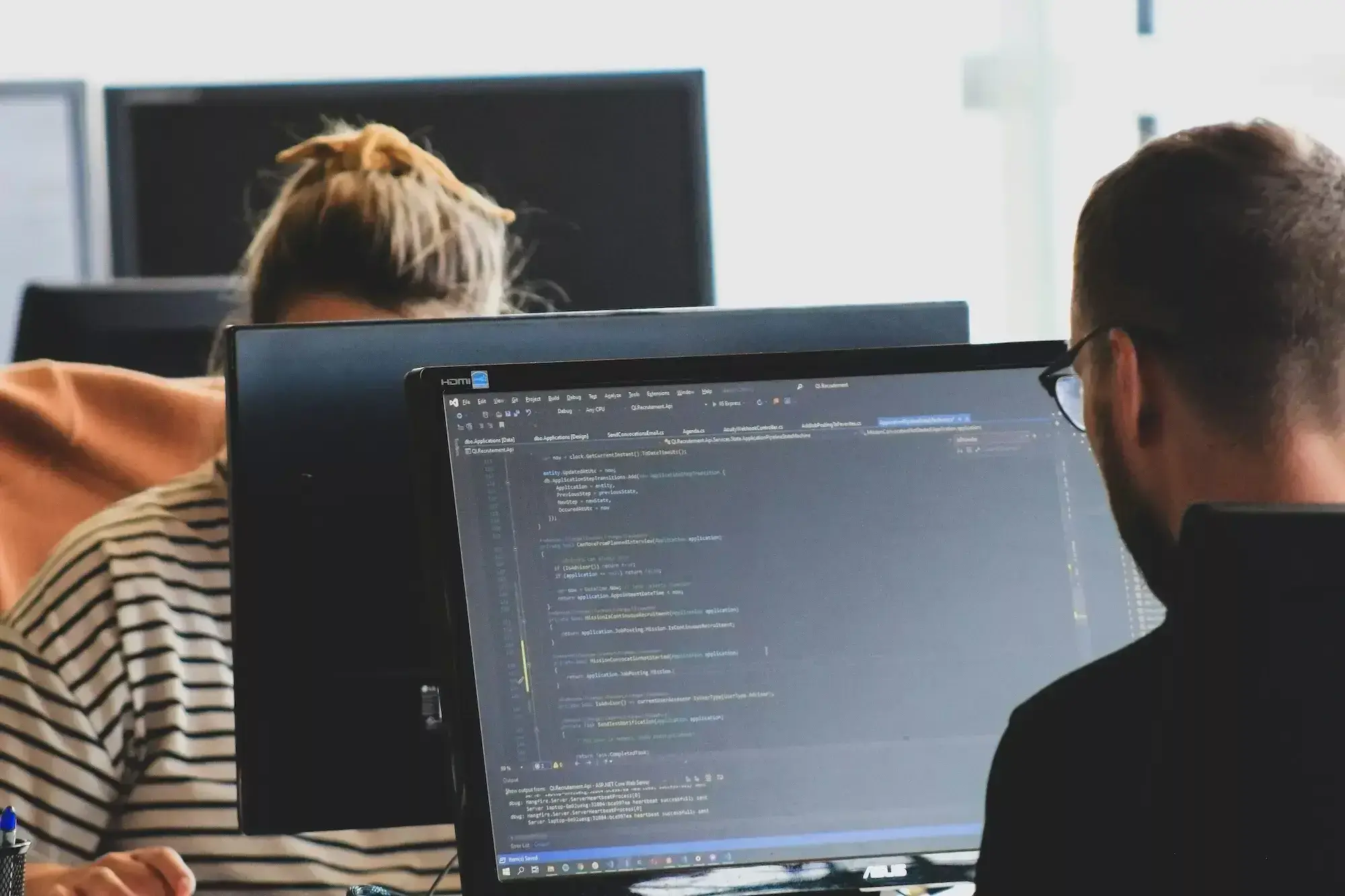 Office workers at monitors, one screen showing code in an editor