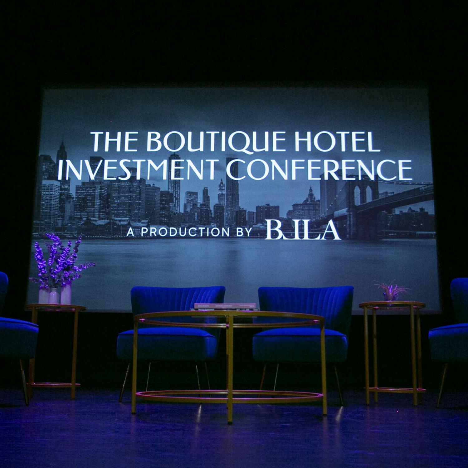 Boutique Hotel Investment Conference stage with chairs and large screen