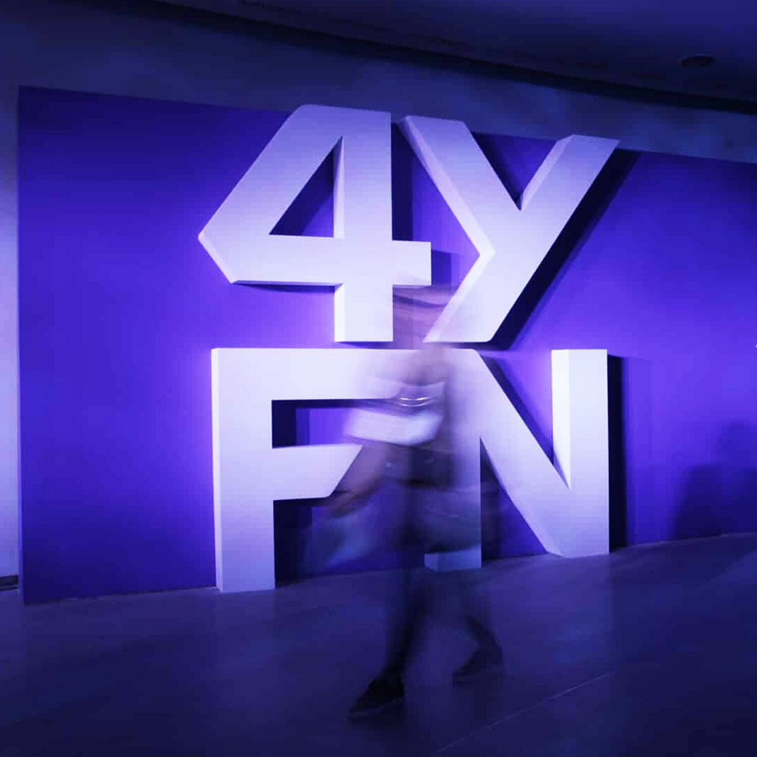 Large 4YFN sign on a purple wall with a blurred person walking past