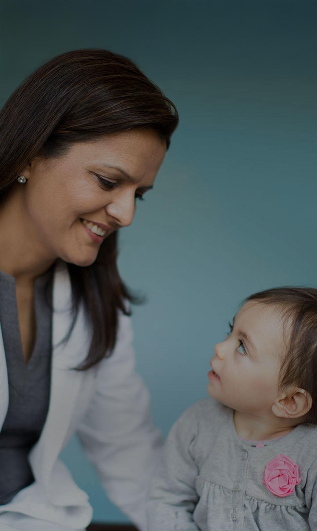 Female doctor smiling at a young child against a teal background