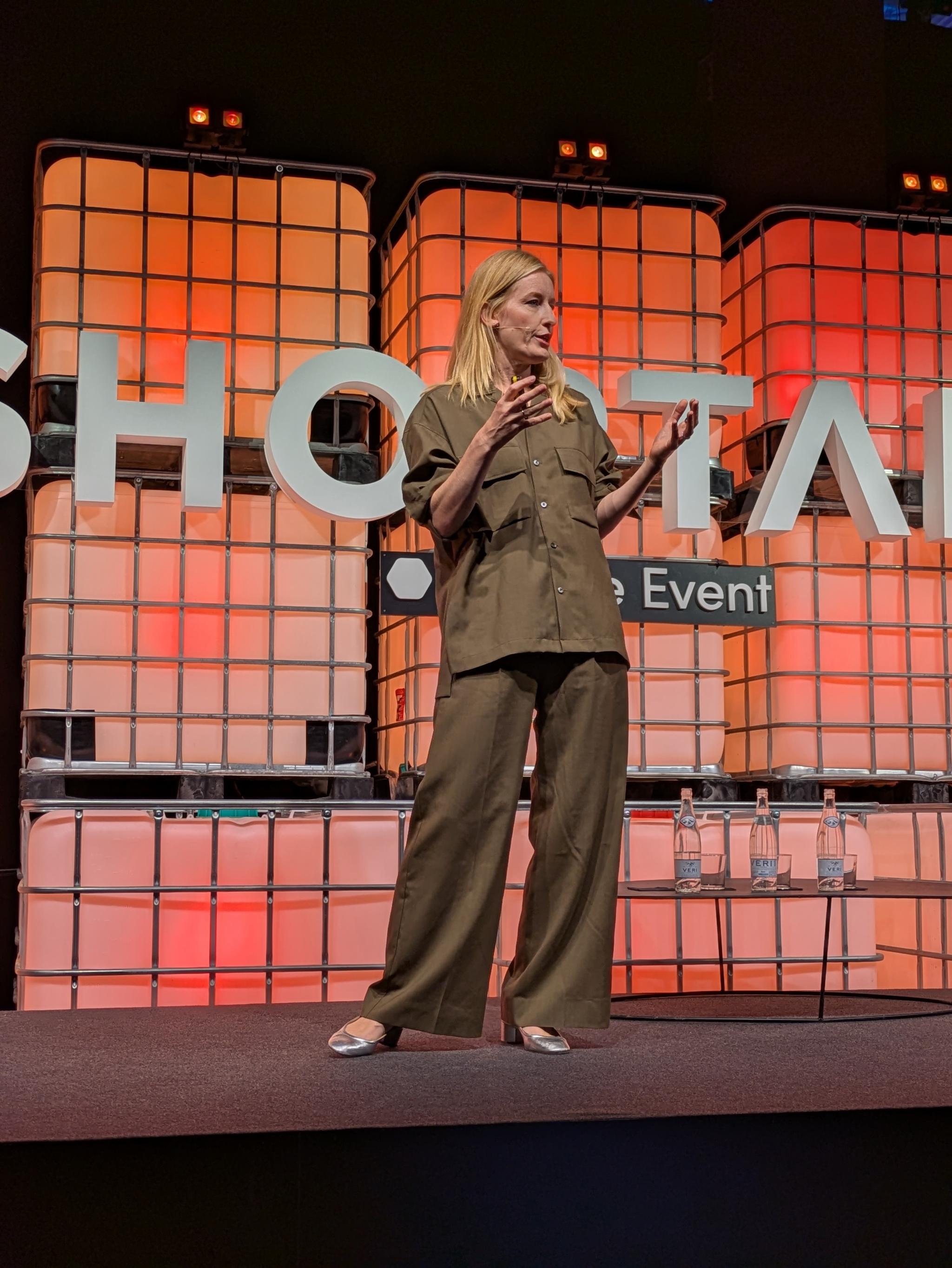 Woman speaking on a Shoptalk stage with orange backdrop