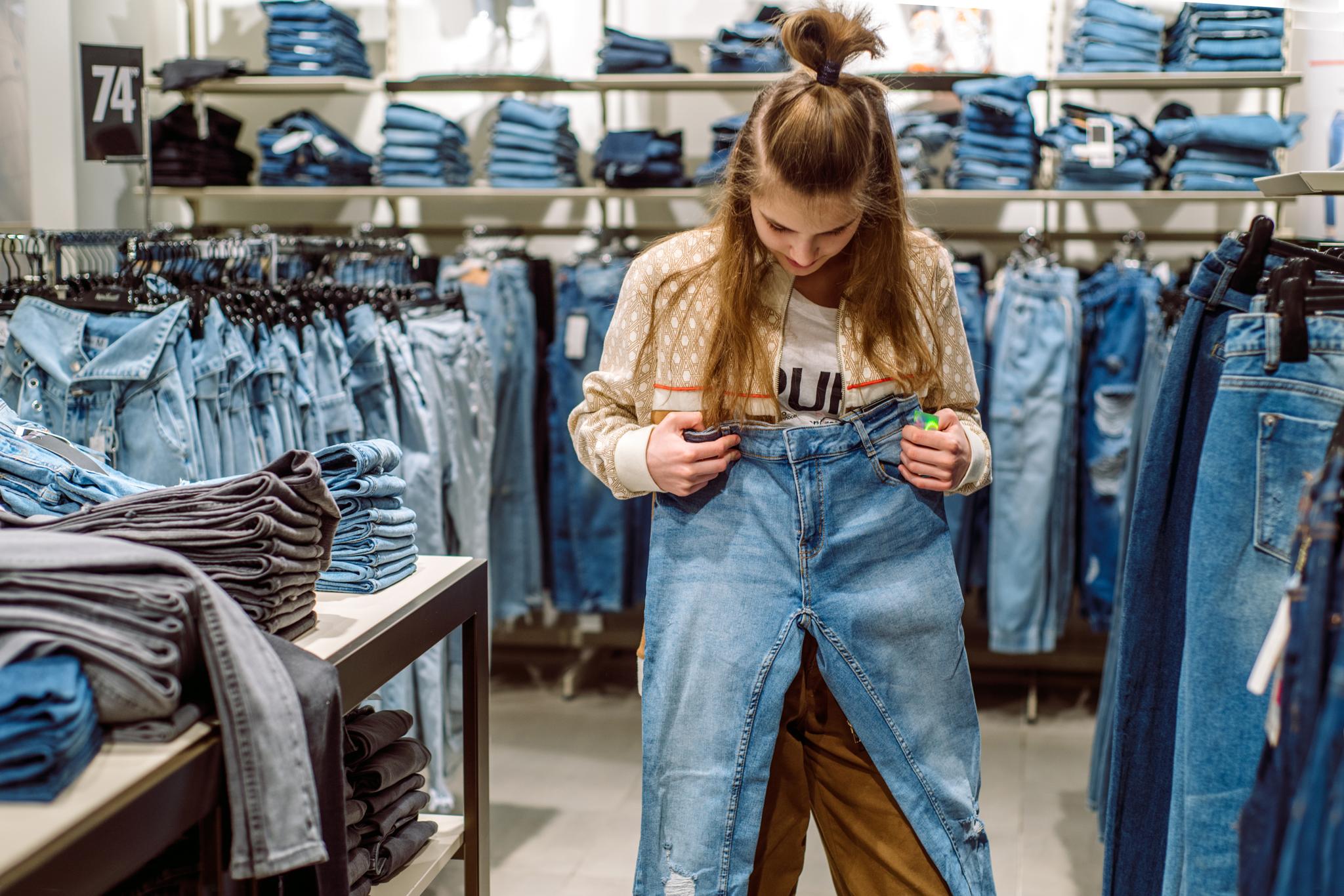 Shopper holding jeans in a denim store aisle