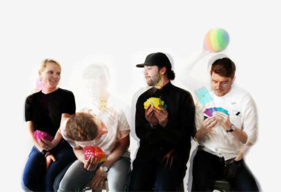 Team 2x 1 Four people sitting against a white wall, holding colorful cards