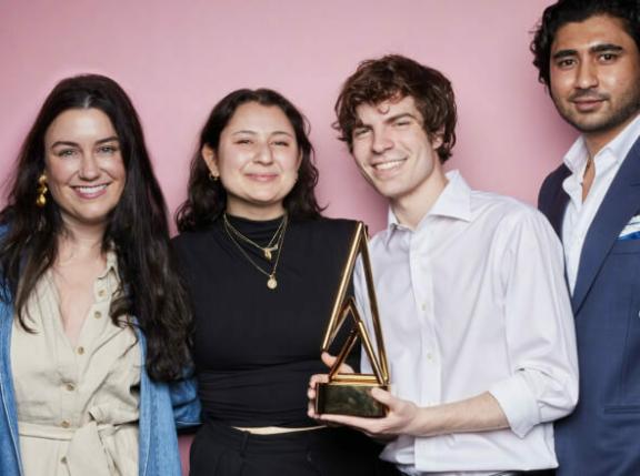 IMG 20230122 123507 Four people posing with a triangular award against a pink backdrop