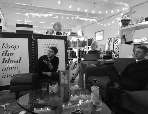 Screen Shot 2023 01 26 at 4 16 2 Three people seated in a creative office lounge with posters and string lights