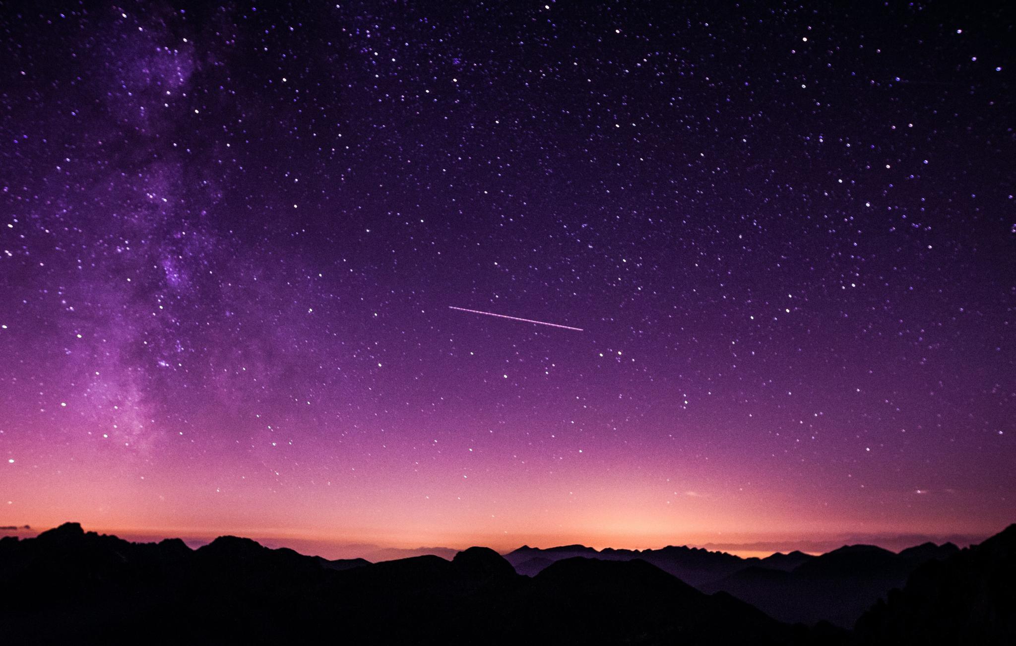 Starry night sky with purple Milky Way over mountain silhouettes