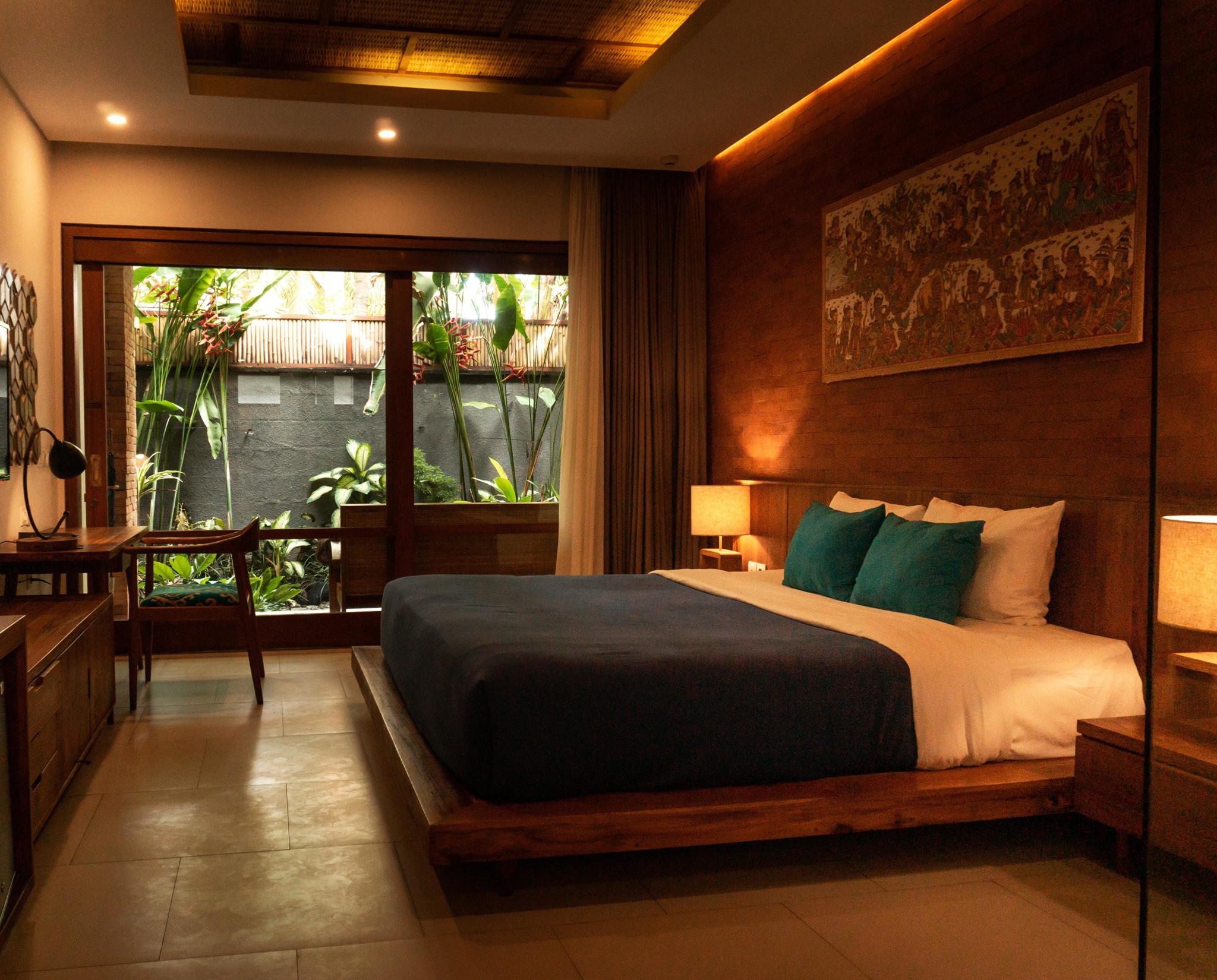 Warmly lit hotel bedroom with a large bed and garden-facing window